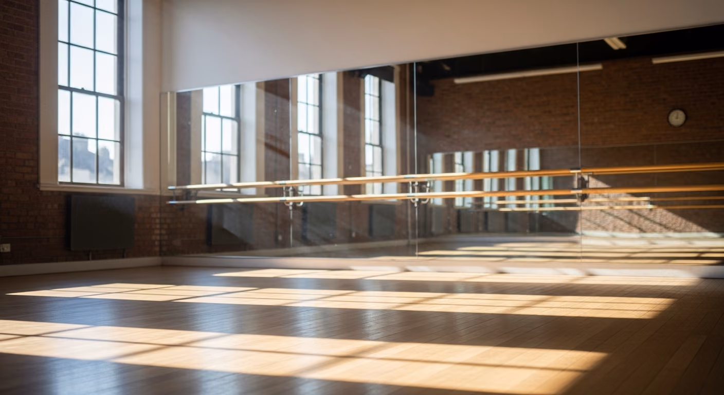Estudio de danza con suelo de madera flotante, pared con espejos y barras de ballet.