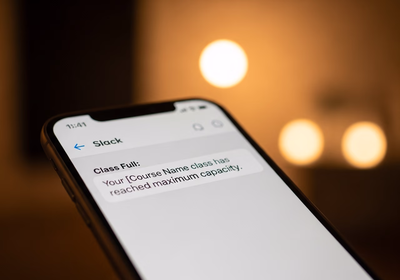 Foto eines Smartphones, das eine Slack-Nachrichtenvorschau mit einer Benachrichtigung über eine ausgefüllte Klasse zeigt, verschwommener Studiohintergrund, warme Farbtöne, keine Logos.